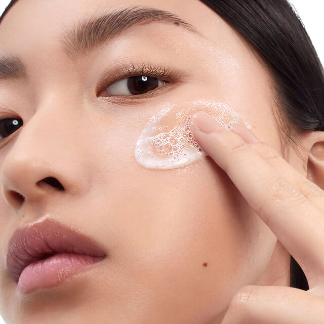 Fair-skinned model Celine applying YSL Pure Shots Clean Reboot Mousse, a foamy cleanser, to her cheek.