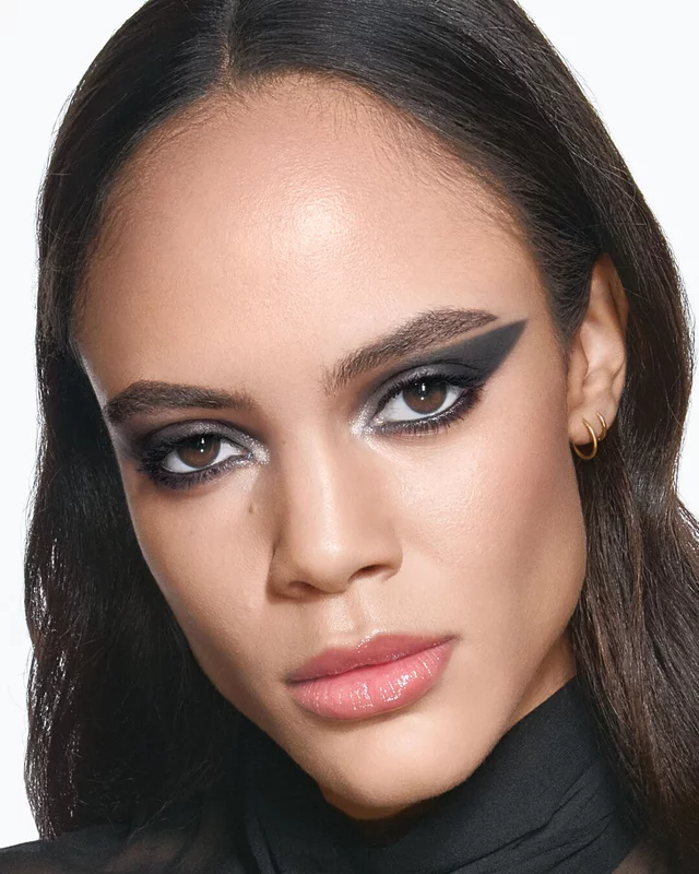 YSL model Kalixte with a bold, graphic black eyeliner look and glossy nude lips, wearing a chic black sheer blouse.