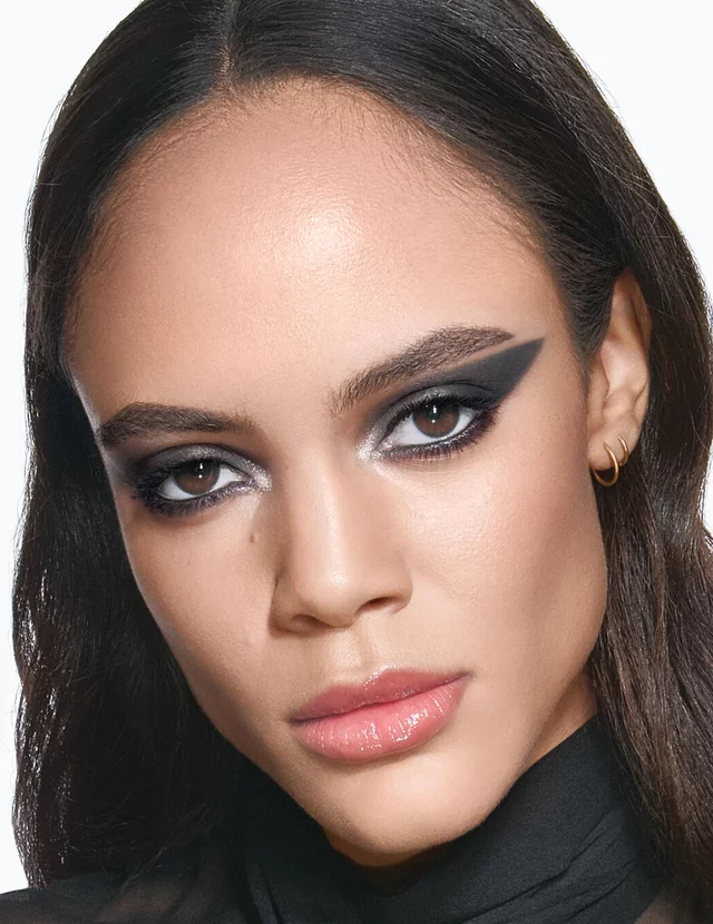 YSL model Kalixte with a bold, graphic black eyeliner look and glossy nude lips, wearing a chic black sheer blouse.