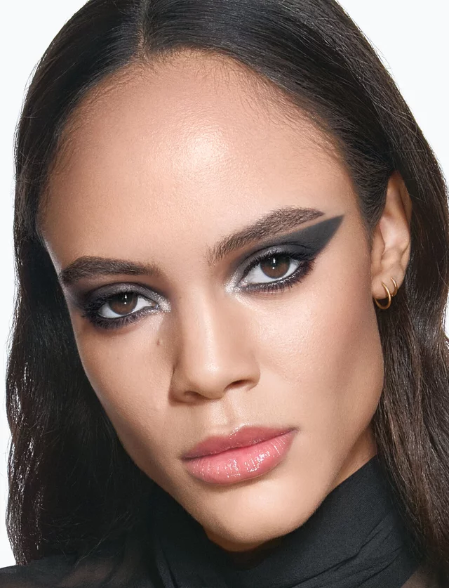 YSL model Kalixte with a bold, graphic black eyeliner look and glossy nude lips, wearing a chic black sheer blouse.