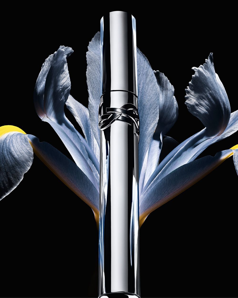 YSL Lash Latex Mascara, sleek silver tube with logo, elegantly placed within a blue iris flower on a dark background.