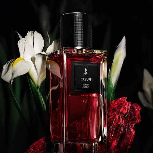COEUR Eau de Parfum by YSL bottle surrounded by noble Iris pallida and red amber on a dark background.