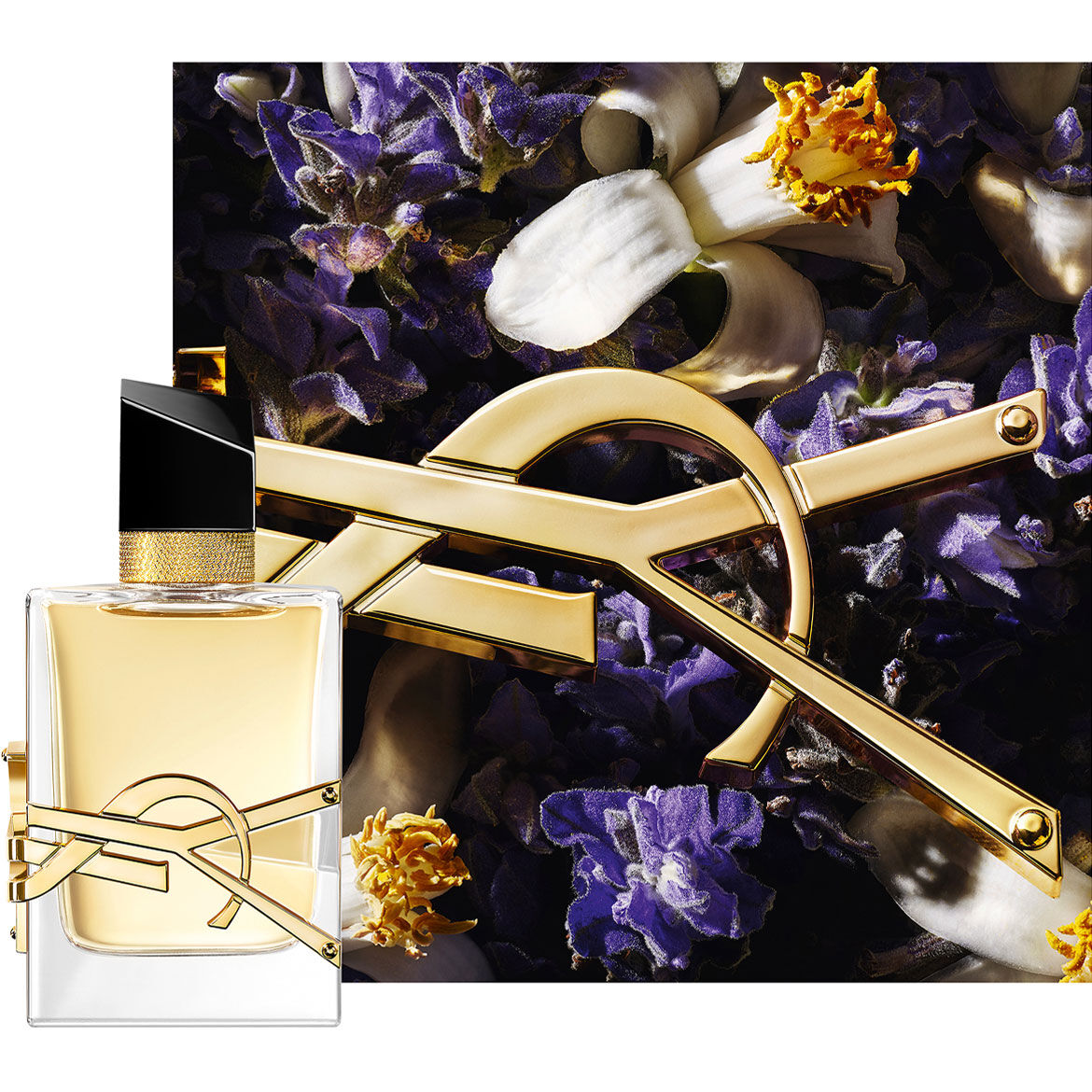 Libre Eau de Parfum bottle styled with gold chain and purple flowers on a dark background.