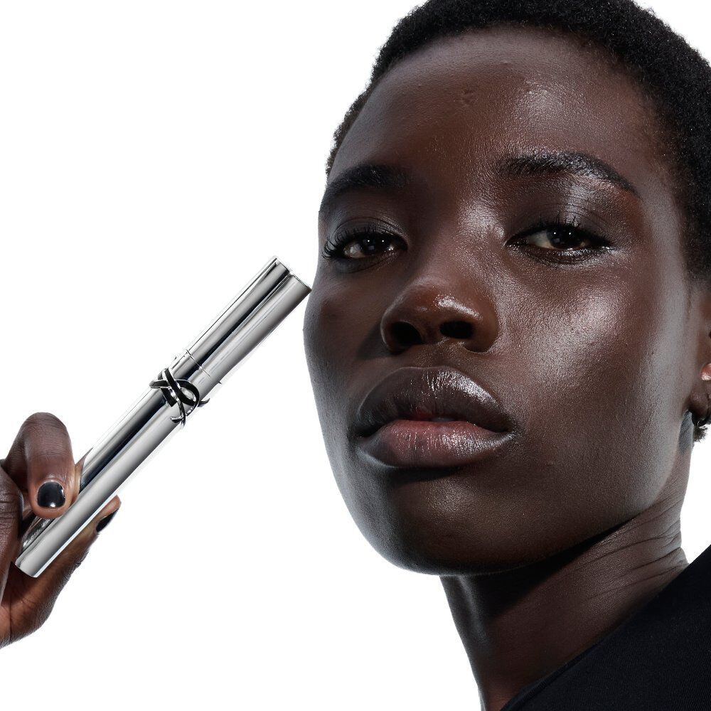 YSL Lash Latex Mascara, held by a model with deep skin tone, showcasing the sleek silver tube.