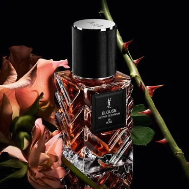 Three-quarter view of YSL LVDP Blouse Extrait de Parfum bottle, with pink roses and thorny stems on a dark background.