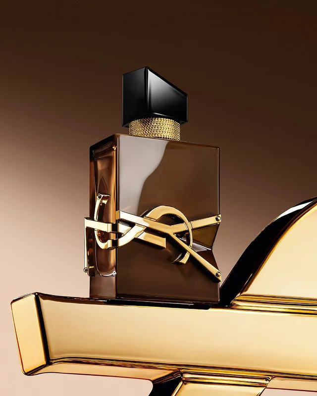 Glazed brown Libre Santal Couture bottle reflecting light, placed on a large golden YSL Cassandre.