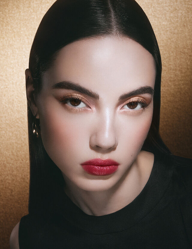 Model with vibrant raspberry makeup look, set against a dark golden background.