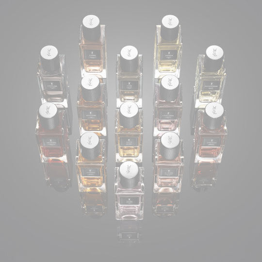 Full collection of YSL Le Vestiaire des Parfums fragrances in clear bottles with black caps, showcasing diverse liquid hues, on a reflective black surface.