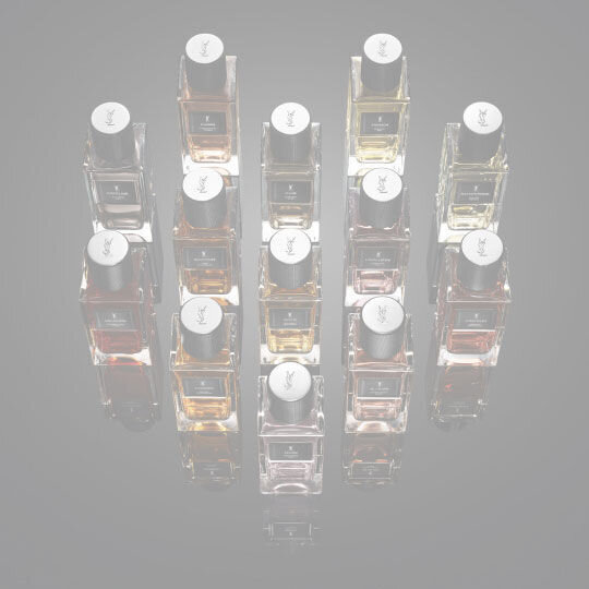 Full collection of YSL Le Vestiaire des Parfums fragrances in clear bottles with black caps, showcasing diverse liquid hues, on a reflective black surface.