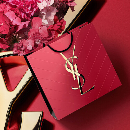 YSL Beauty pink shopping bag, golden Cassandre logo, textured, amidst vibrant pink florals. Mother's Day elegance