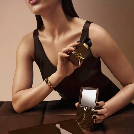 Model in a brown couture dress holding Libre Santal Couture and a matching glazed brown mirror.