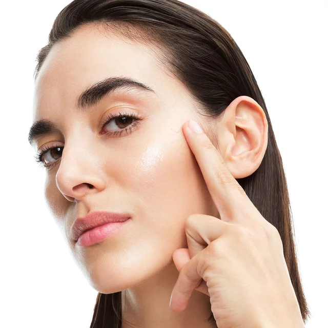 Alicia, YSL Beauty model, applying YSL Pure Shots Stability Reboot to her cheek, highlighting skin's natural glow.