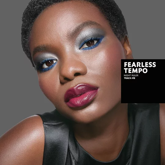 Marie, dark skin tone, with a fearless tempo eye look featuring silver and blue, and glossy berry lips.