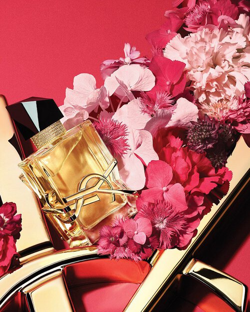 YSL LIBRE Eau de Parfum bottle on a glossy gold YSL logo, with vibrant pink flowers, against a pink background.