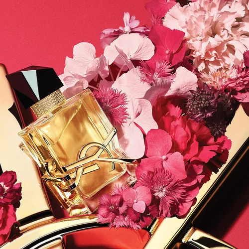 YSL LIBRE Eau de Parfum bottle on a glossy gold YSL logo, with vibrant pink flowers, against a pink background.