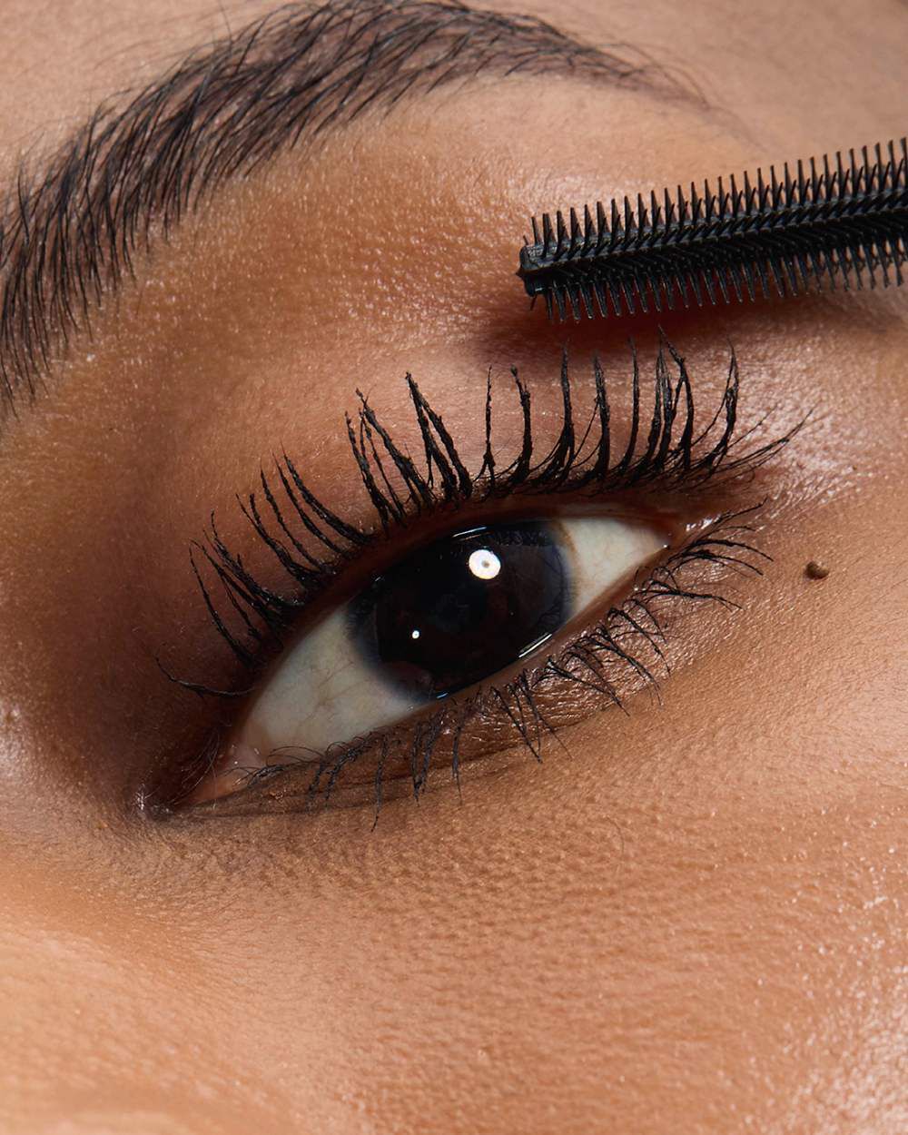 Close-up of an eye with medium skintone, showing YSL Lash Latex Mascara in shade 1 with a brush focus, applied to lashes.