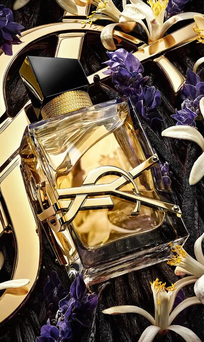 Libre Eau de Parfum lying on fresh lavender and orange blossoms with a golden YSL Cassandre background.