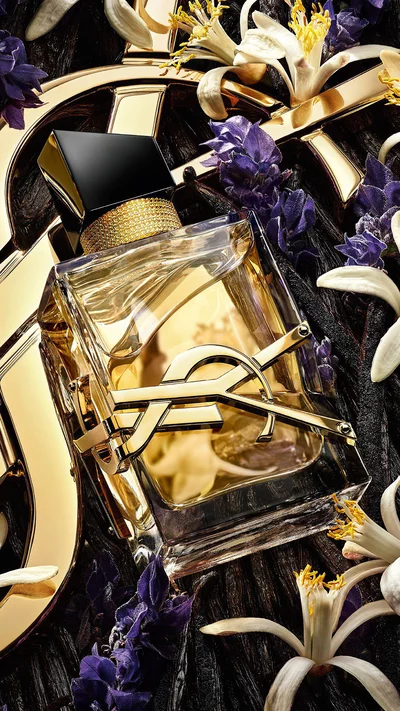 Libre Eau de Parfum lying on fresh lavender and orange blossoms with a golden YSL Cassandre background.