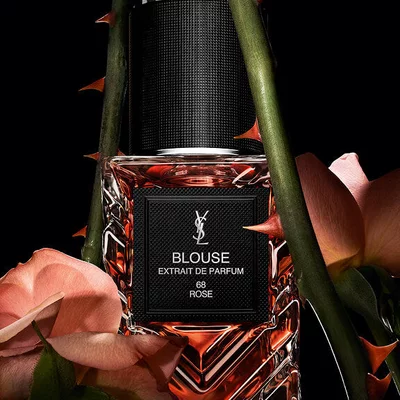 YSL LVDP Blouse Extrait de Parfum bottle, elegantly framed by delicate pink roses and thorny stems on a dark background.