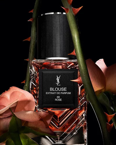 YSL LVDP Blouse Extrait de Parfum bottle, elegantly framed by delicate pink roses and thorny stems on a dark background.
