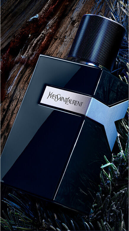 YSL Y Le Parfum bottle, dark blue with silver Y logo, on a rustic  wooden background with dark green pine needles.