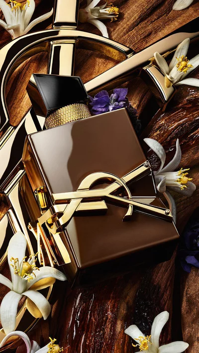 Libre Santal Couture bottle on raw sandalwood bark with a golden YSL Cassandre in the background.