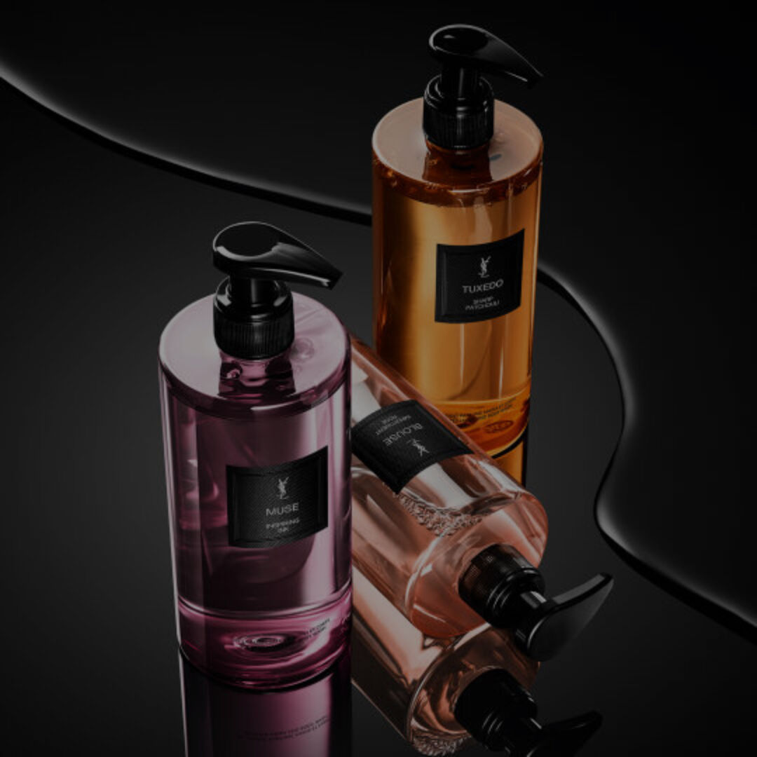 Le Vestiaire des Parfums Bath & Body Collection: three pump bottles—pink (Muse), amber (Tuxedo), and nude (Blouse)—on a glossy black surface with fluid reflections.