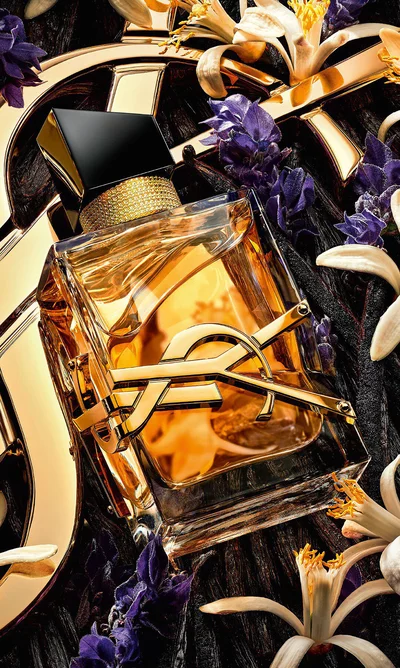 Libre Eau de Parfum Intense lying on lavender and orange blossoms with a golden YSL Cassandre in the background.