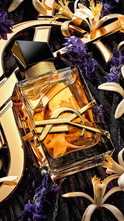 Libre Eau de Parfum Intense lying on lavender and orange blossoms with a golden YSL Cassandre in the background.