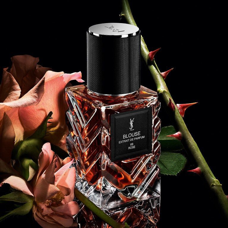 Three-quarter view of YSL LVDP Blouse Extrait de Parfum bottle, with pink roses and thorny stems on a dark background.