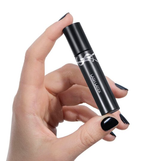 Hand with black nail polish holding YSL Beauty Lash Latex Mascara, against a white background.