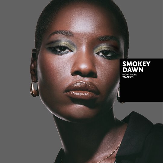 Awar, deep skin tone, with a smokey dawn eye look featuring green and gold, and glossy brown lips.