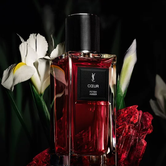 COEUR Eau de Parfum by YSL bottle surrounded by noble Iris pallida and red amber on a dark background.