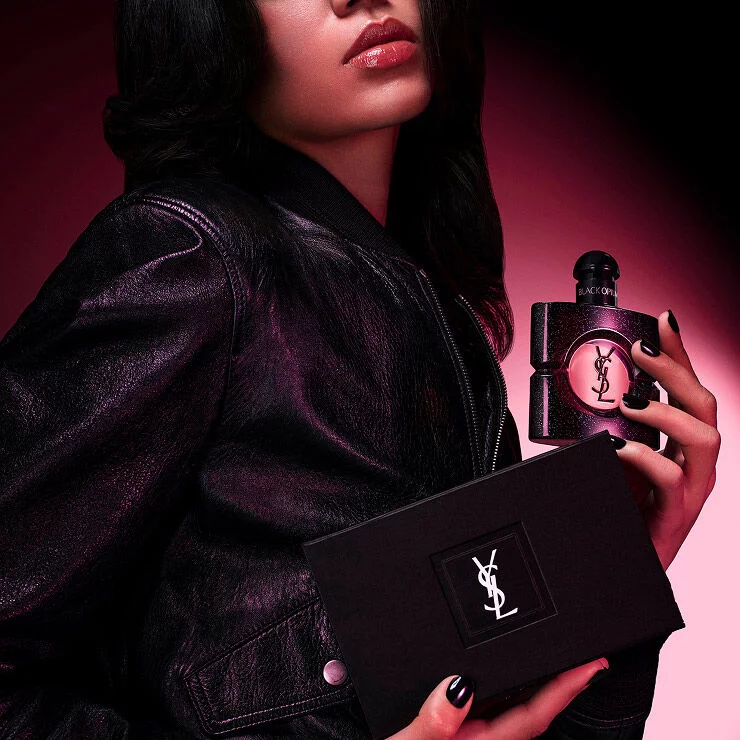 A women model in a leather jacket holding a Black Opium Eau de Parfum bottle and a black YSL gift box.