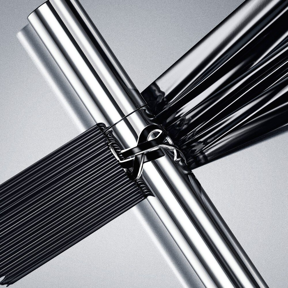 Two high-shine silver YSL Lash Latex Mascara tubes crossed over thick, glossy black mascara strokes.