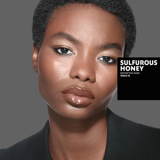 Marie, dark skin tone, with an instinctive nude eye look and sulfurous honey glossy lips, wearing a black blazer.