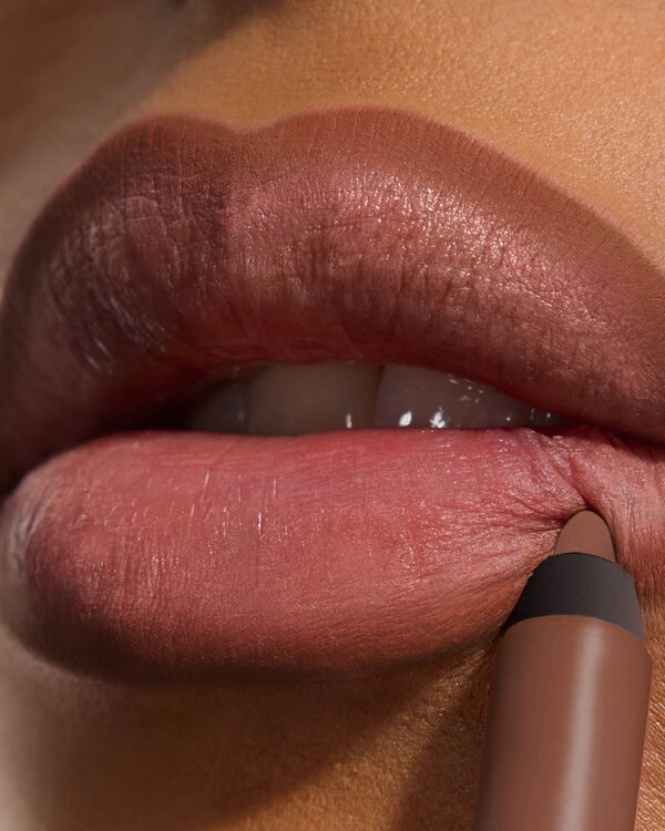 Bineta applying YSL LOVENUDE Kiss Shaper 26 in Shade 109, a close- up of her lips.