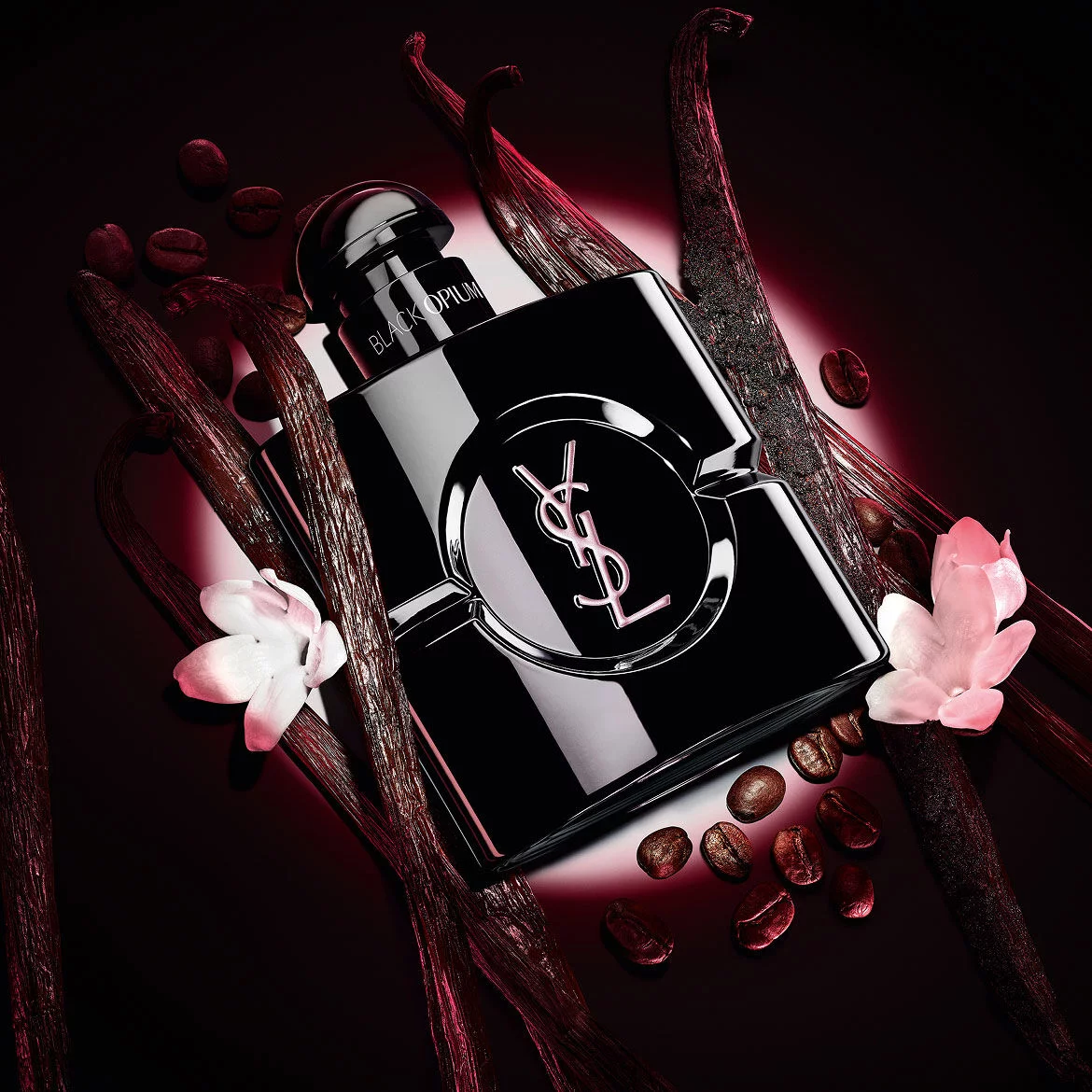 Black Opium Le Parfum bottle in glossy black, surrounded by dark vanilla pods and white jasmine.