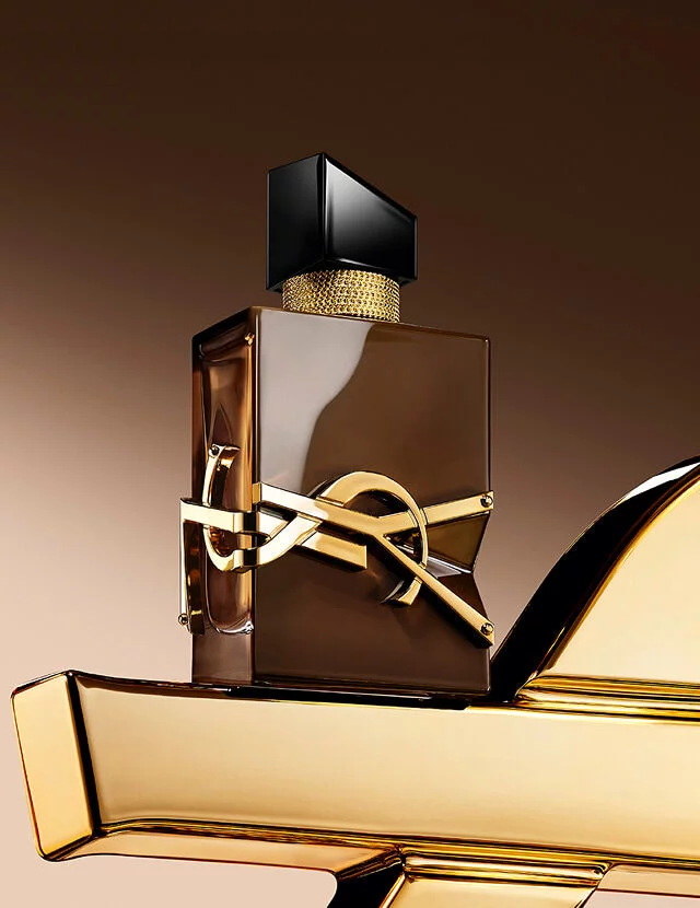 Glazed brown Libre Santal Couture bottle reflecting light, placed on a large golden YSL Cassandre.