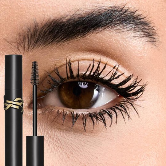 Close-up of an eye with medium skin tone, showcasing volumized lashes from YSL Lash Clash Mascara, with the black tube and golden YSL logo visible.