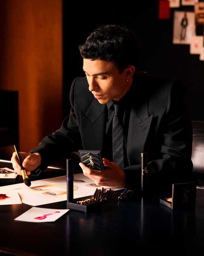 YSL Beauty makeup artist Sam Visser applying luxury makeup, surrounded by YSL products on a dark, elegant surface.
