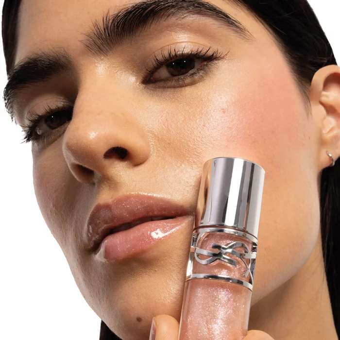 YSL Beauty model, holding YSL LOVESHINE Plumping Lip Oil Gloss shade 10, applied on her lips, medium skin.