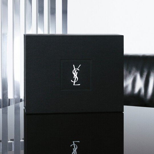 YSL Beauty black gift box with iconic YSL logo, presented on a reflective black surface with metallic accents.