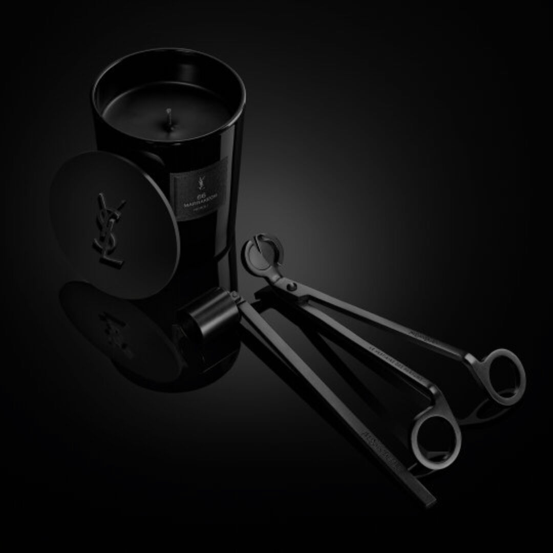 Le Vestiaire des Parfums Home Scent Collection: black candle with YSL lid and wick trimmer tools on a glossy dark surface.