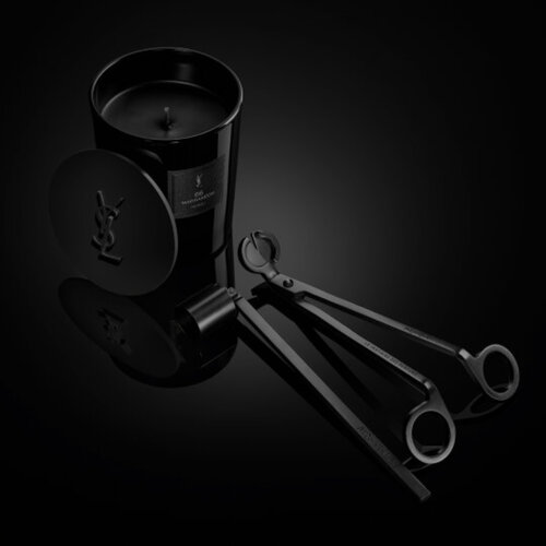 Le Vestiaire des Parfums Home Scent Collection: black candle with YSL lid and wick trimmer tools on a glossy dark surface.