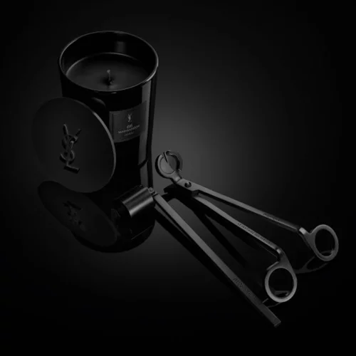 Le Vestiaire des Parfums Home Scent Collection: black candle with YSL lid and wick trimmer tools on a glossy dark surface.
