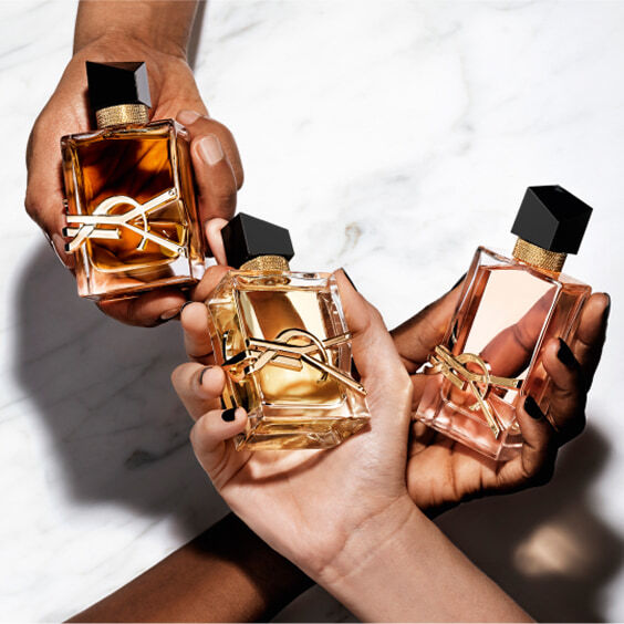 Three hands hold YSL LIBRE Eau de Parfum Intense, Eau de Parfum, and Eau de Toilette, on a white marble.