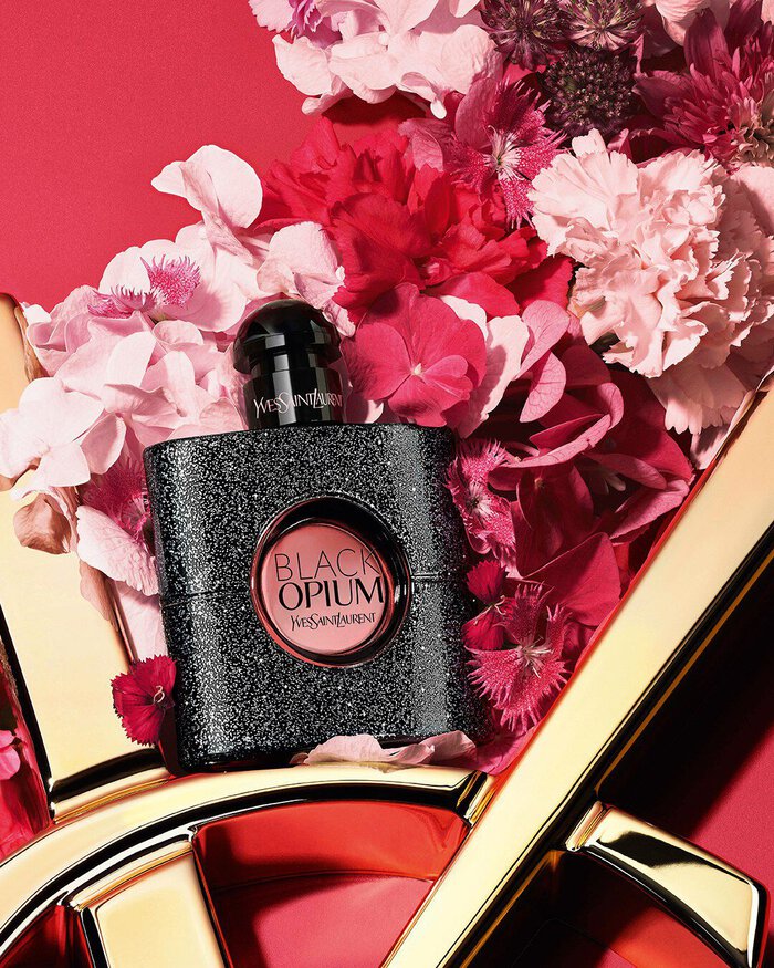 YSL LIBRE Eau de Parfum bottle on a glossy gold YSL logo, with vibrant pink flowers, against a pink background.