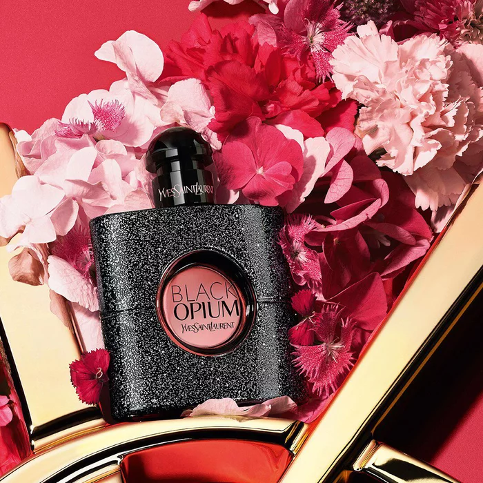 YSL LIBRE Eau de Parfum bottle on a glossy gold YSL logo, with vibrant pink flowers, against a pink background.