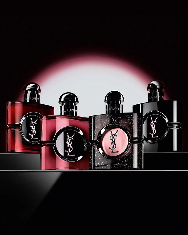 Four different Black Opium perfume bottles displayed in a row on a dark, reflective surface.